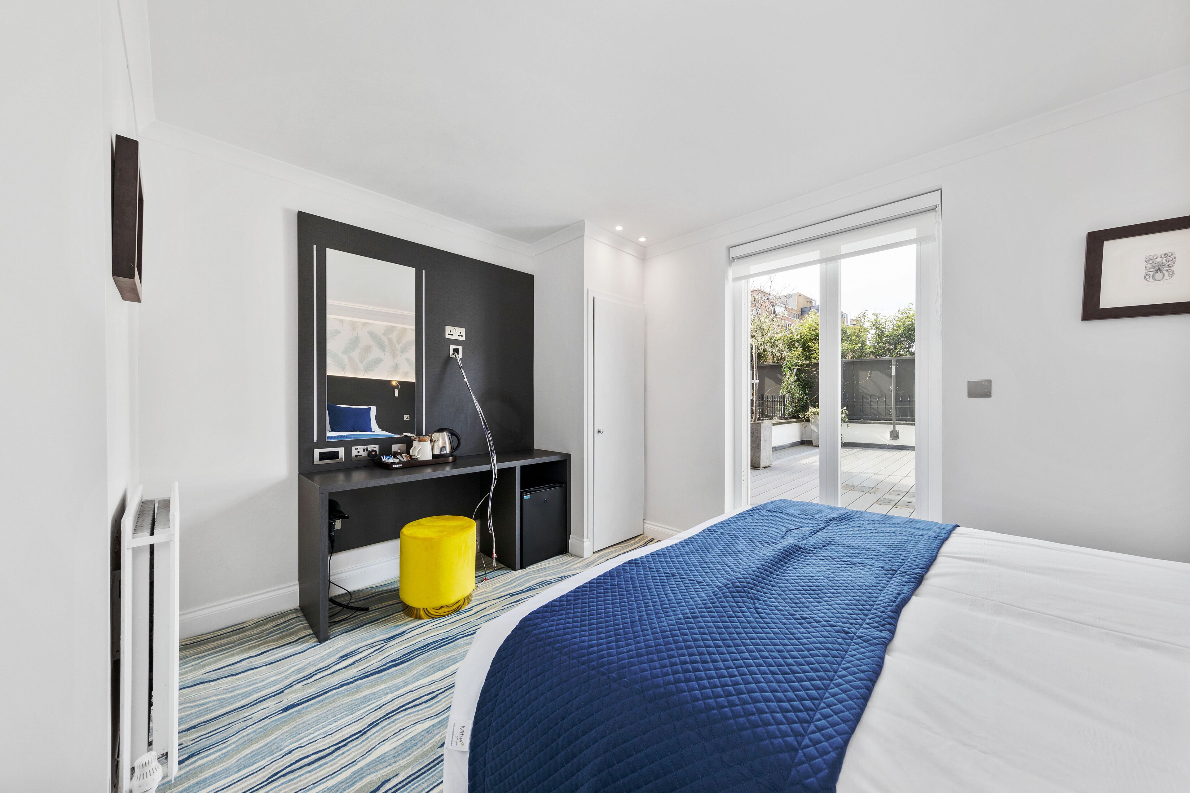 A modern bedroom with a large bed, a desk with a computer, a chair, and a yellow trash bin.