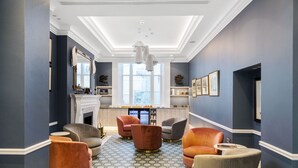 A spacious lounge area with a fireplace, comfortable seating, and a large window providing natural light. - Commodore Hotel (London)