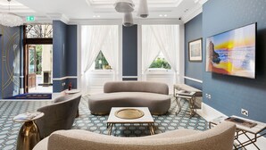 A modern lobby with a blue and white color scheme, featuring a large sofa, a coffee table, and a TV mounted on the wall. - Commodore Hotel (London)