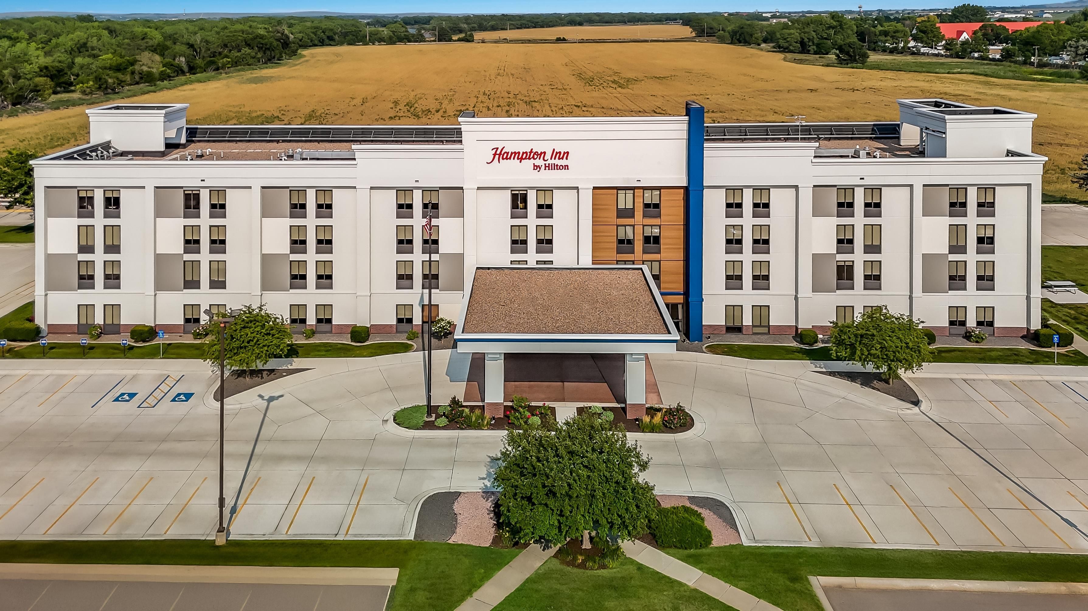 A Hampton Inn by Hilton with a parking lot and a large field in the background.