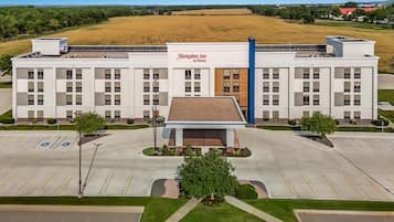 A Hampton Inn by Hilton with a parking lot and a large field in the background.