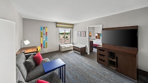 A modern hotel room with a sofa, a small table, a TV, a desk, and a window with a view. - Hampton Inn North Platte (North Platte)