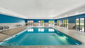 An indoor swimming pool with clear blue water, surrounded by black chairs and tables, and large windows offering views of the outdoors. - Hampton Inn North Platte (North Platte)