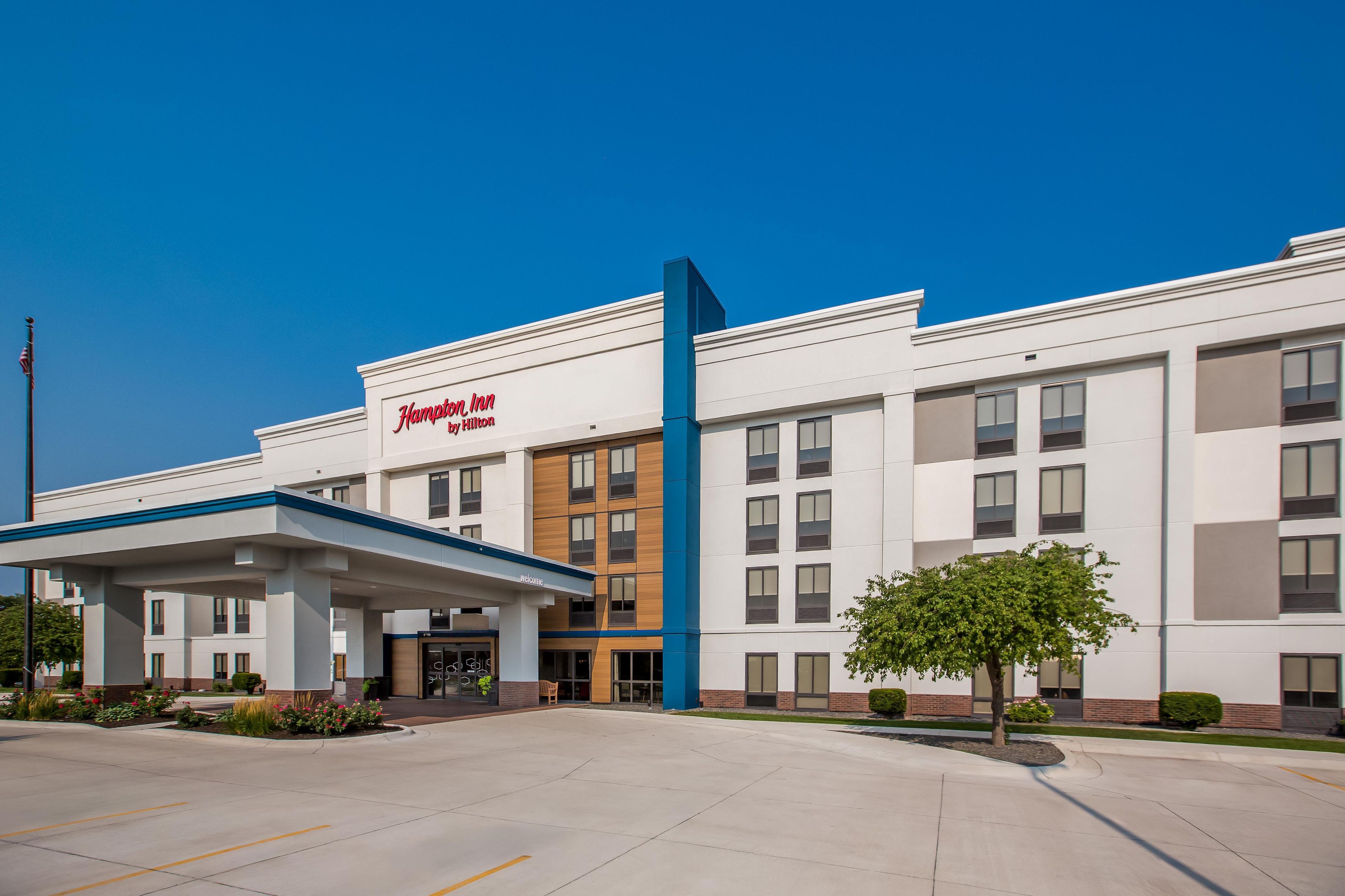 Un hotel Hampton Inn by Hilton con fachada moderna, acceso cubierto y estacionamiento.