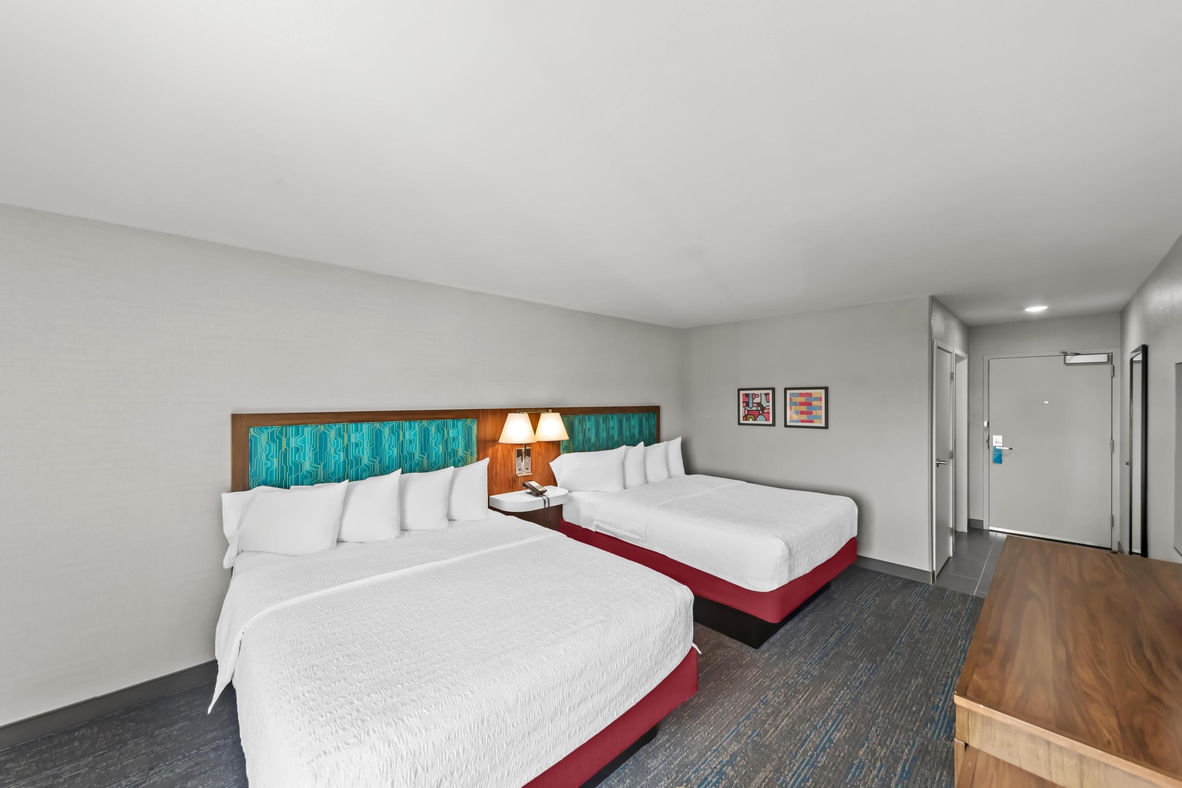 A hotel room with two beds, a wooden desk, and a door leading to a bathroom.