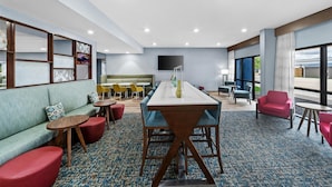 A modern hotel lobby with a long dining table, comfortable seating, and a large window offering a view. - Hampton Inn North Platte (North Platte)