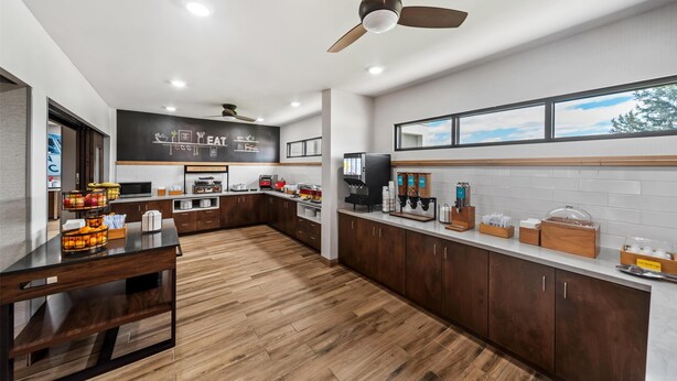 A modern kitchen with wooden cabinets, a blackboard menu, and a fruit display. - Hampton Inn North Platte (North Platte)