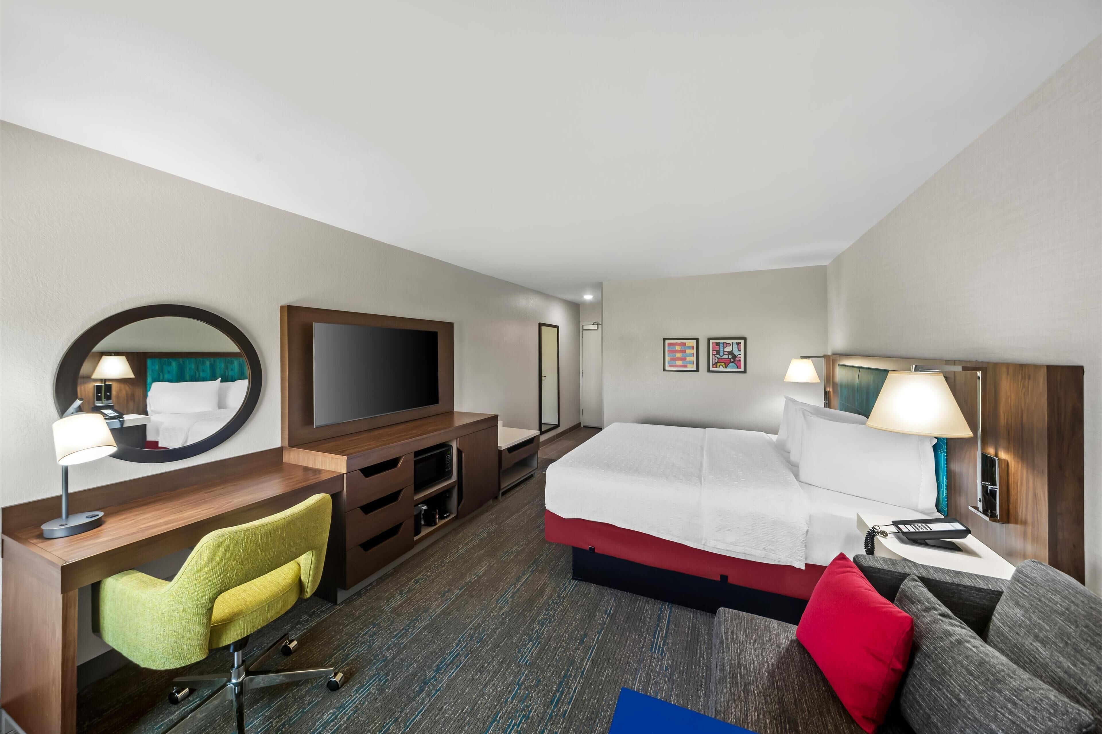 A hotel room with a bed, a desk with a chair, a television, and a mirror.