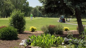 A golf course with a well-maintained lawn, a golf cart, and a person in a green shirt and white shorts. - Holiday Inn Washington-Dulles International Airport by IHG (Sterling)