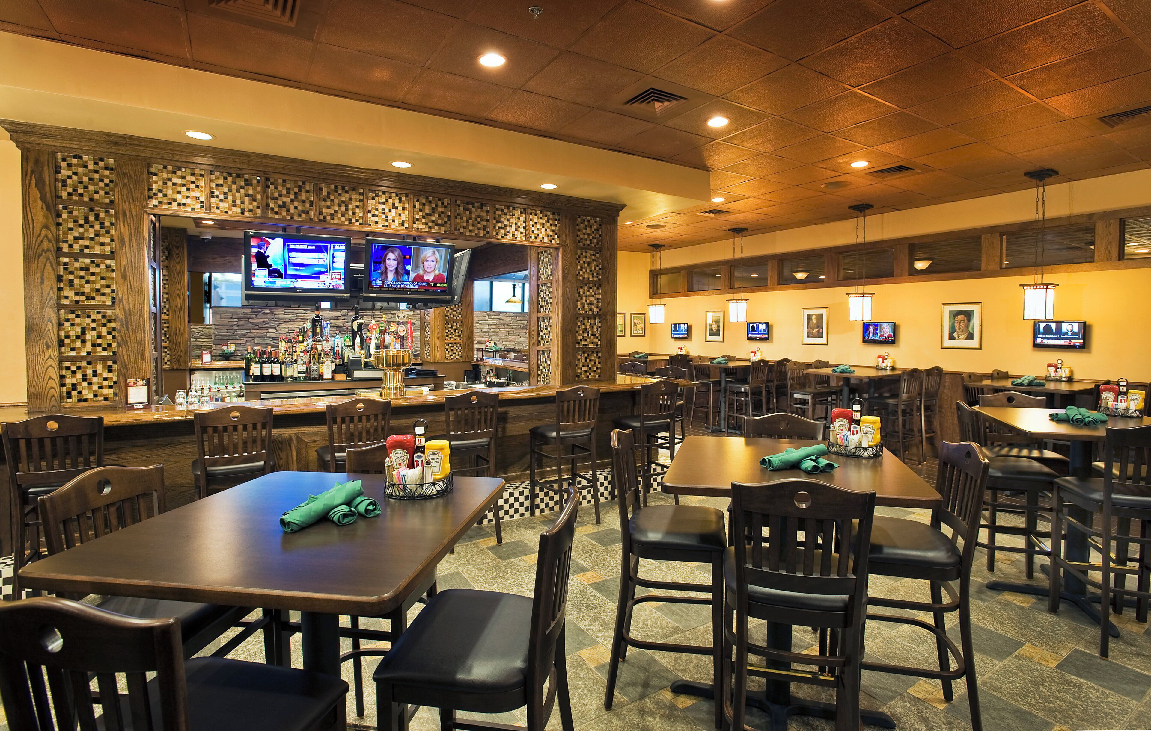 A restaurant with multiple tables and chairs, a bar area with a variety of bottles, and several televisions mounted on the walls.