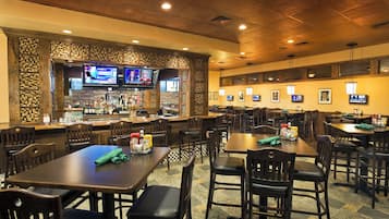A restaurant with multiple tables and chairs, a bar area with a variety of bottles, and several televisions mounted on the walls.