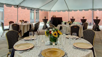 A tented outdoor dining area with tables set for a meal, featuring chairs and table settings.