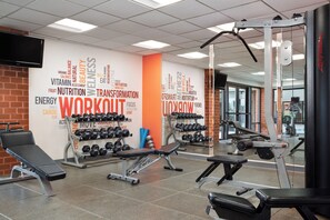 Uma academia com diversos equipamentos de exercício, uma parede com palavras motivacionais e uma televisão fixada na parede.