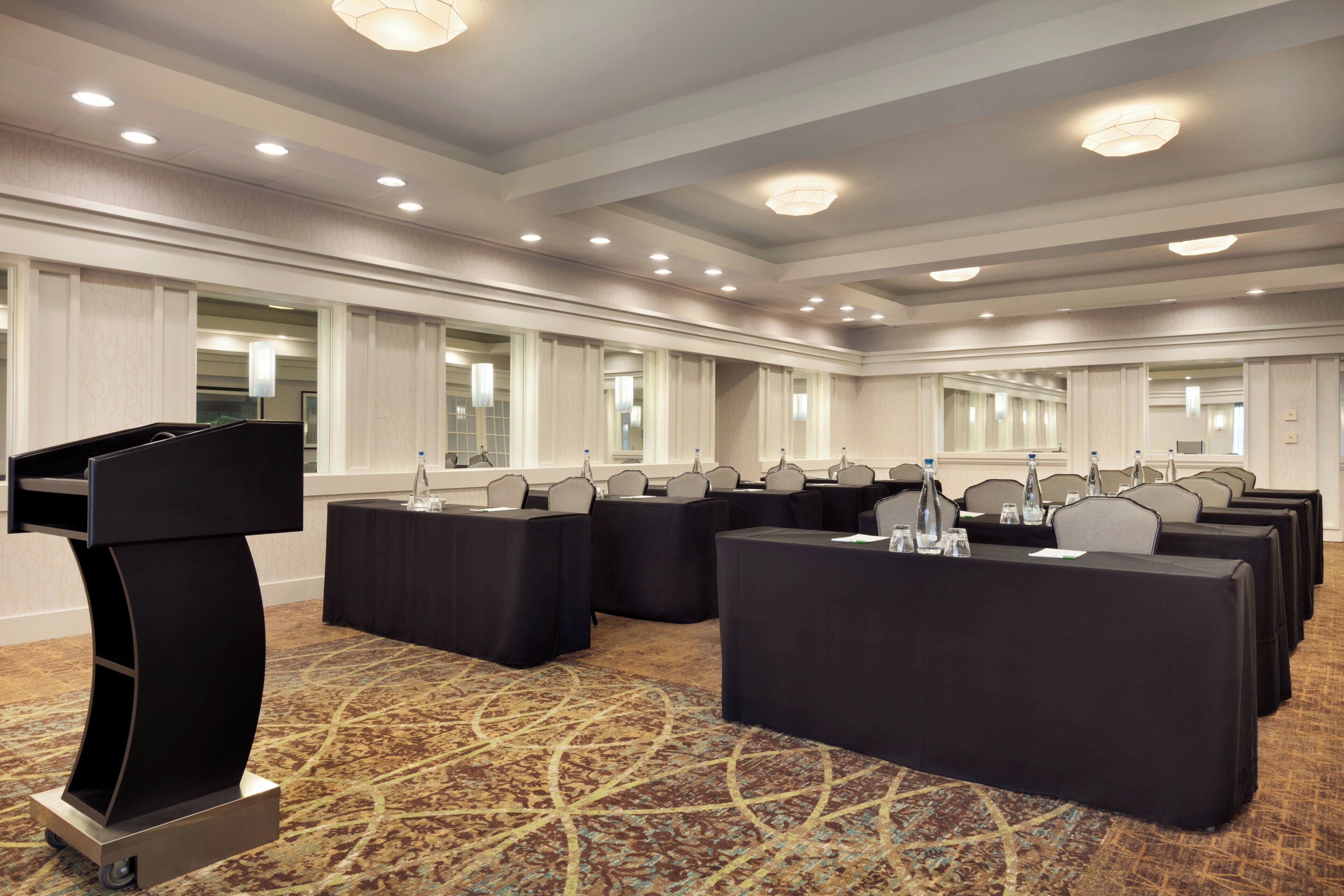 A conference room with multiple tables, a podium, and a carpeted floor.