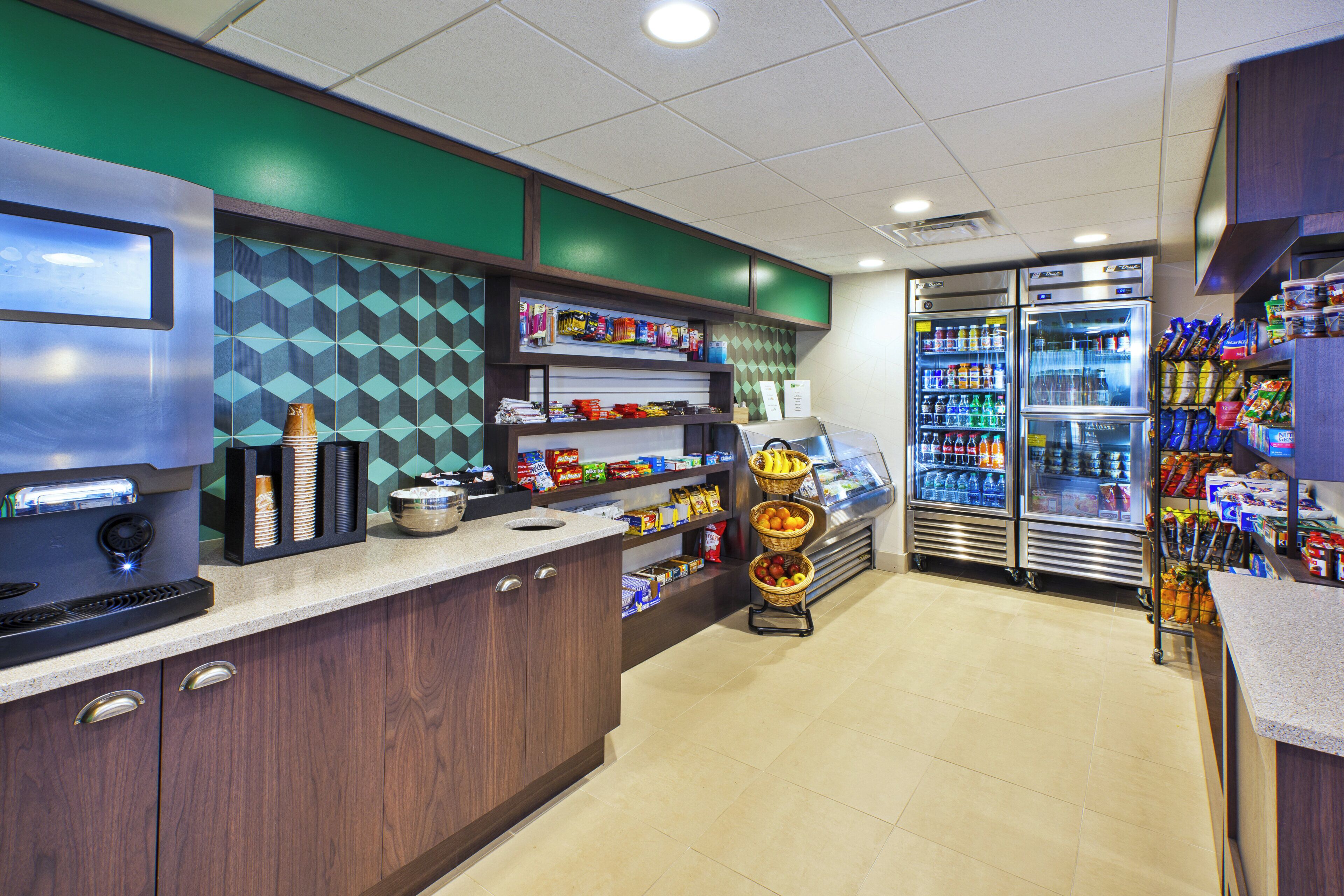 Una estación de bebidas de autoservicio con dispensadores refrigerados y una selección de bocadillos.