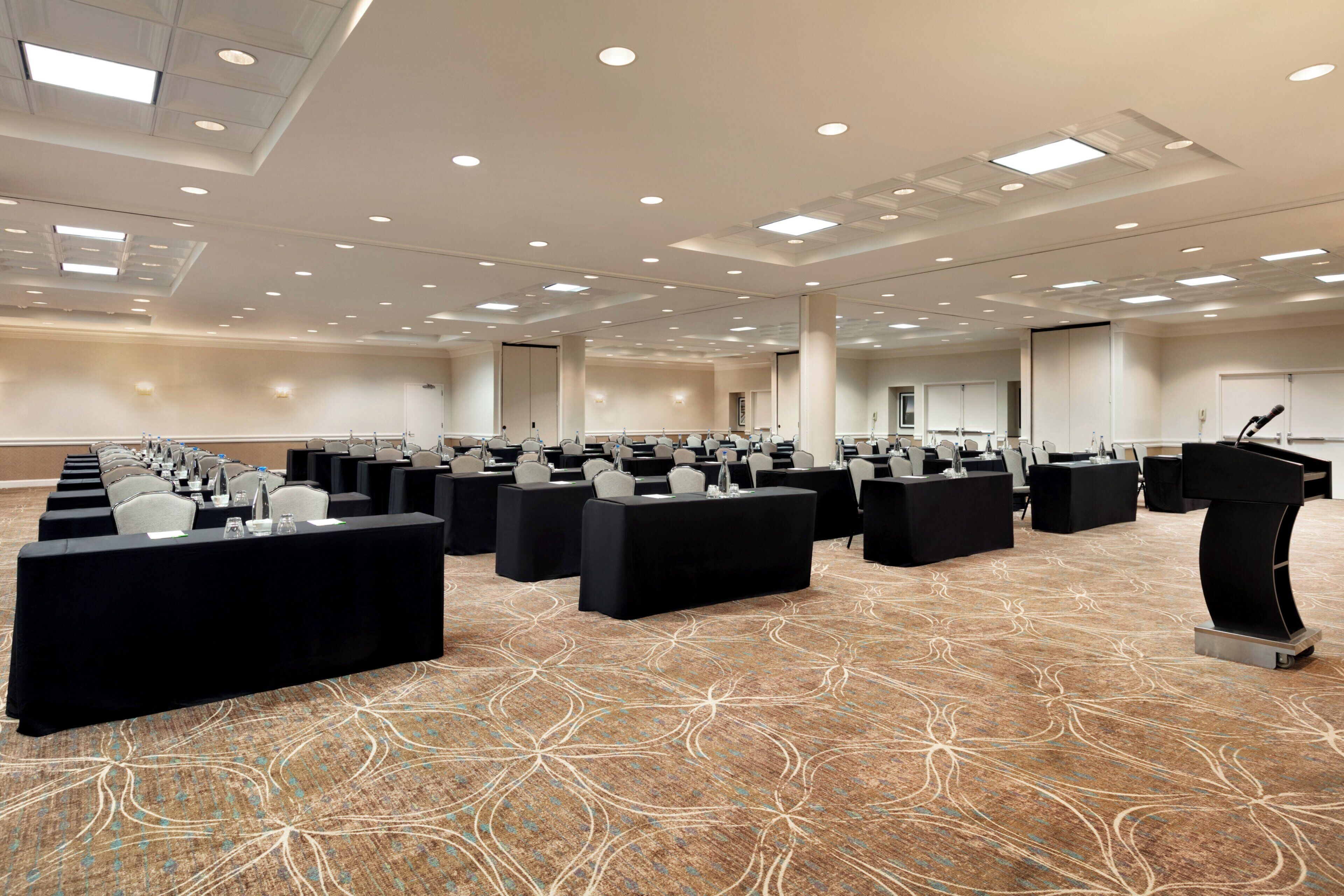 Un salón de conferencias con filas de mesas y sillas, equipado con micrófonos y botellas de agua.