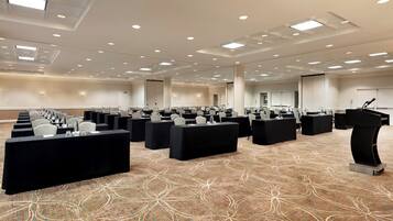 Un salón de conferencias con filas de mesas y sillas, equipado con micrófonos y botellas de agua.