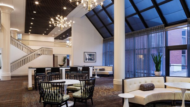 A spacious lobby with a high ceiling, a staircase, a seating area with a sofa and chairs, and a large window with curtains. - Holiday Inn Washington-Dulles International Airport by IHG (Sterling)