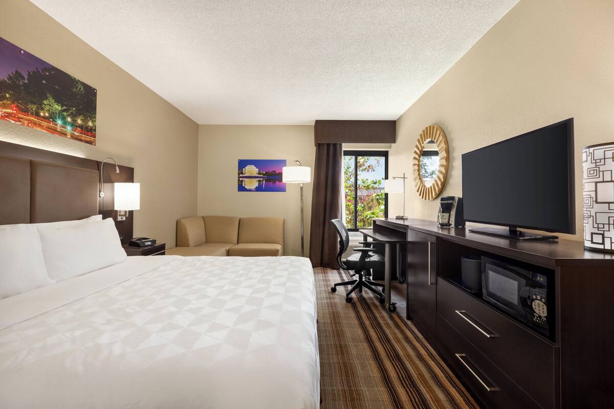 A hotel room with a large bed, a desk with a computer, a television, and a painting on the wall.
