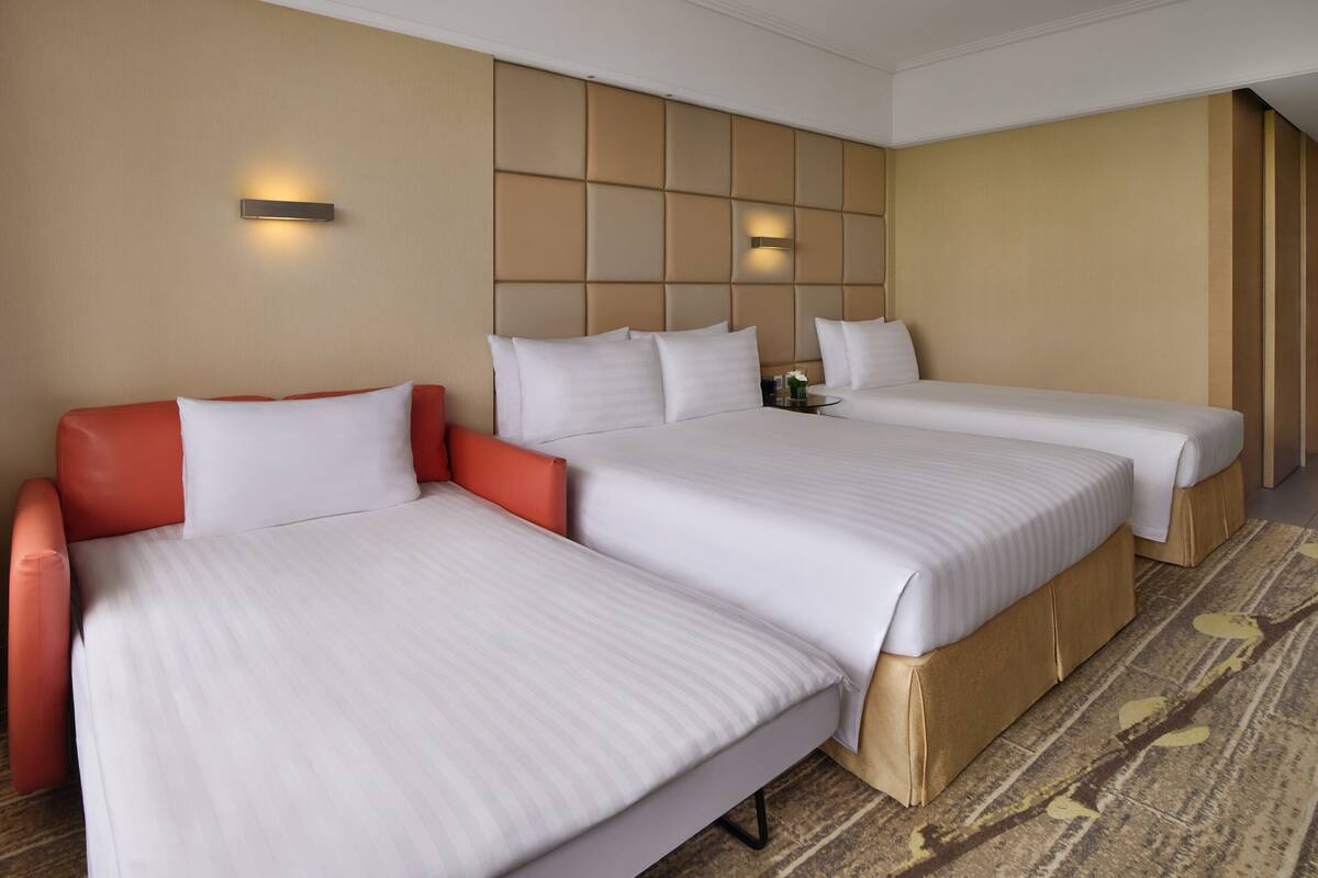 A hotel room with two beds, a red sofa, and a decorative wall panel.