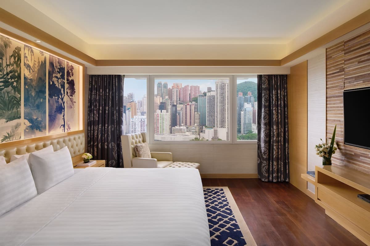 A hotel room with a large bed, a city view, a TV, and a wooden panel wall.