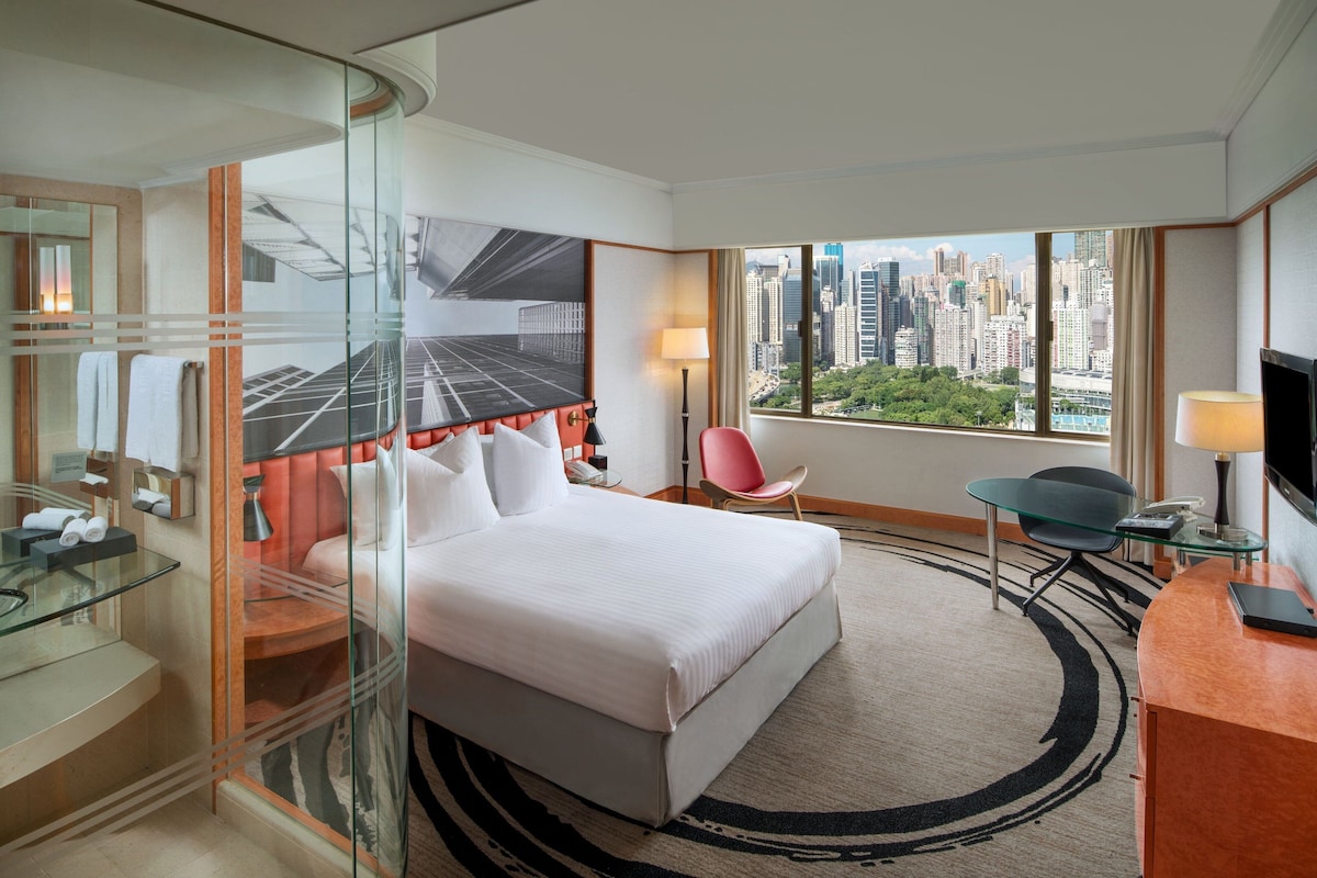 A hotel room with a bed, a desk, a chair, a TV, and a large window with a city view.