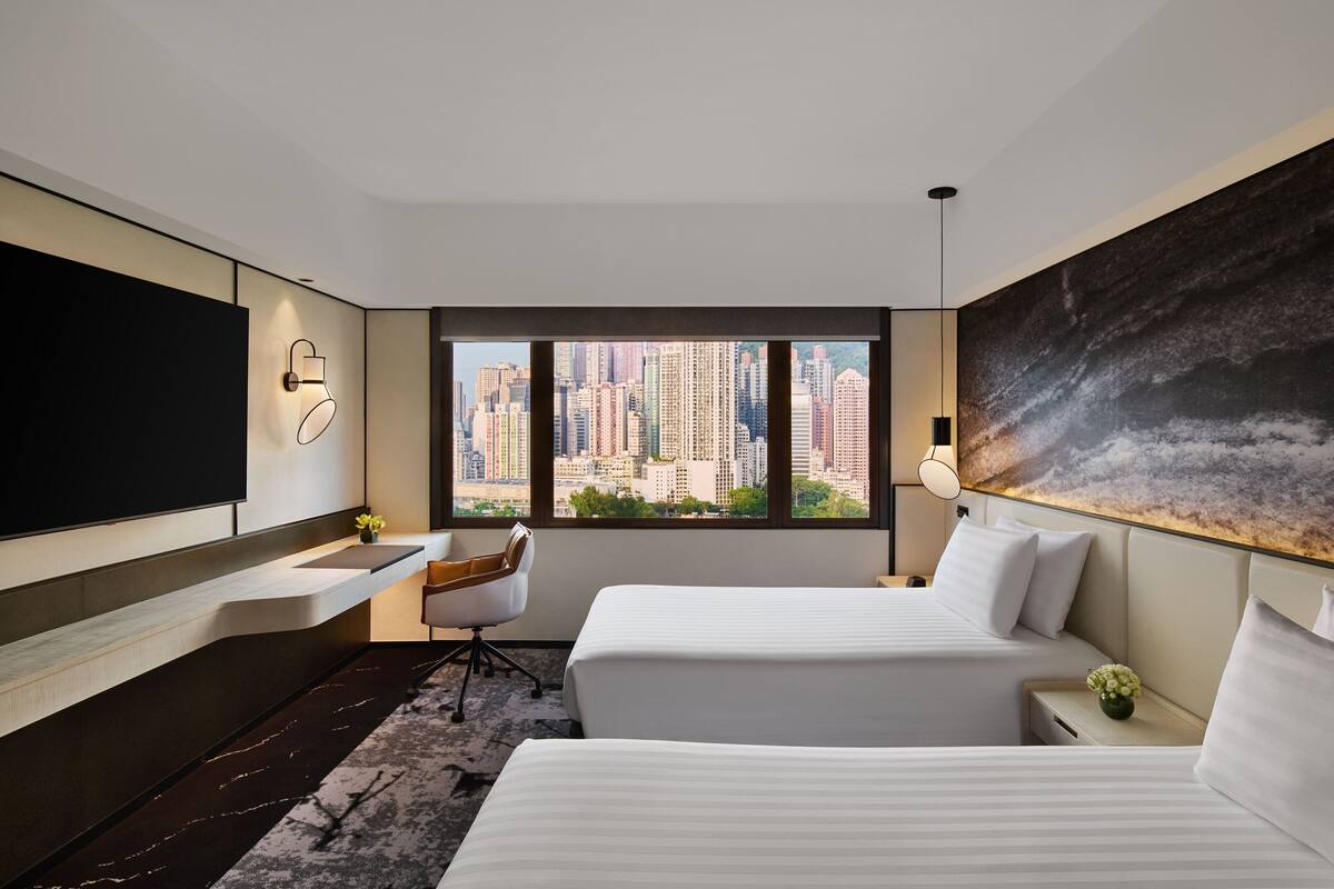 A modern hotel room with a city view, a flat-screen TV, a desk, and two beds.