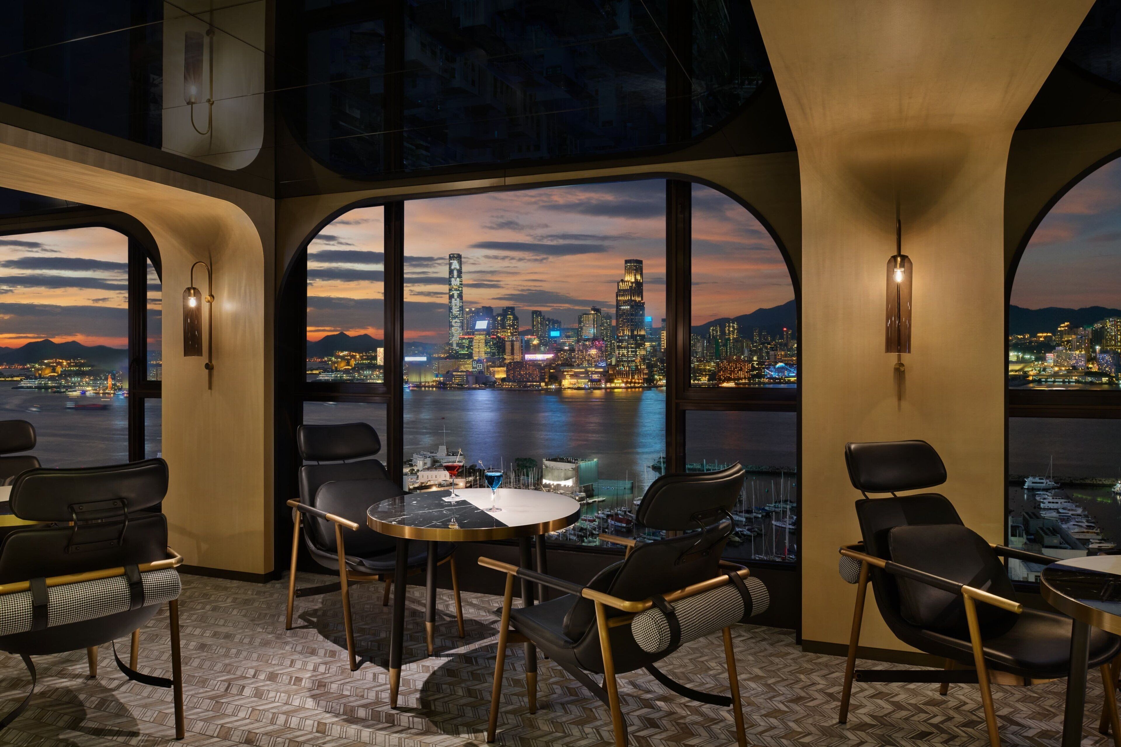 A modern interior with large arched windows offering a cityscape view at dusk.