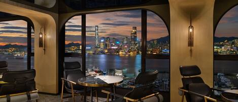 A modern interior with large arched windows offering a cityscape view at dusk.
