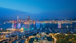 A marina with numerous boats docked, a city skyline in the background, and buildings with flat roofs in the foreground. - The Park Lane Hong Kong, Autograph Collection (Hong Kong)