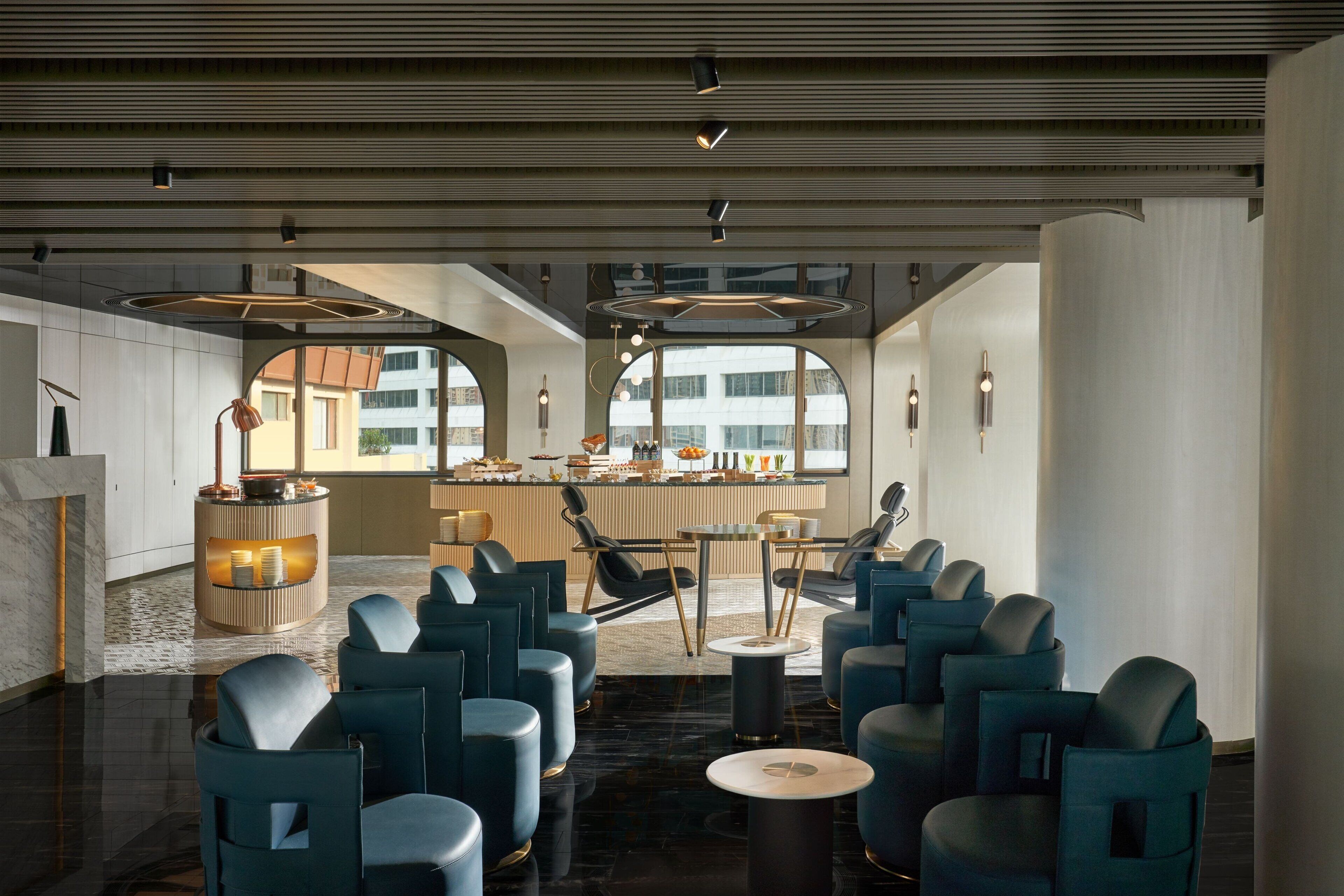 Um lobby moderno de hotel com área de estar, balcão de recepção e grandes janelas com vista para a cidade.