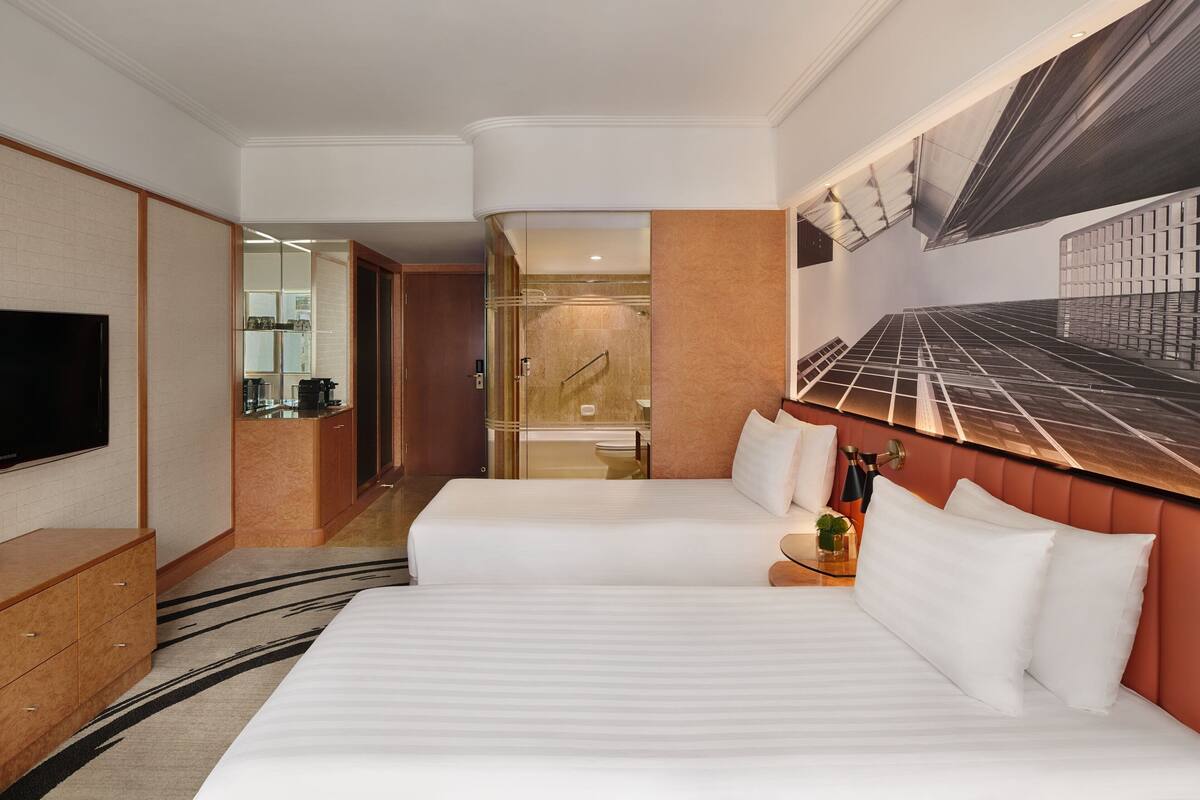 A hotel room with a large bed, a TV, a desk, and a bathroom visible through a glass door.