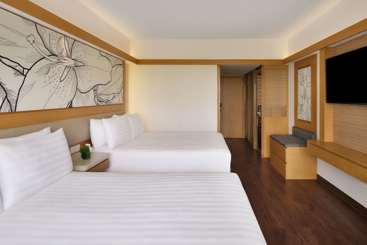 A hotel room with two beds, a TV, wooden flooring, and a large floral artwork on the wall.