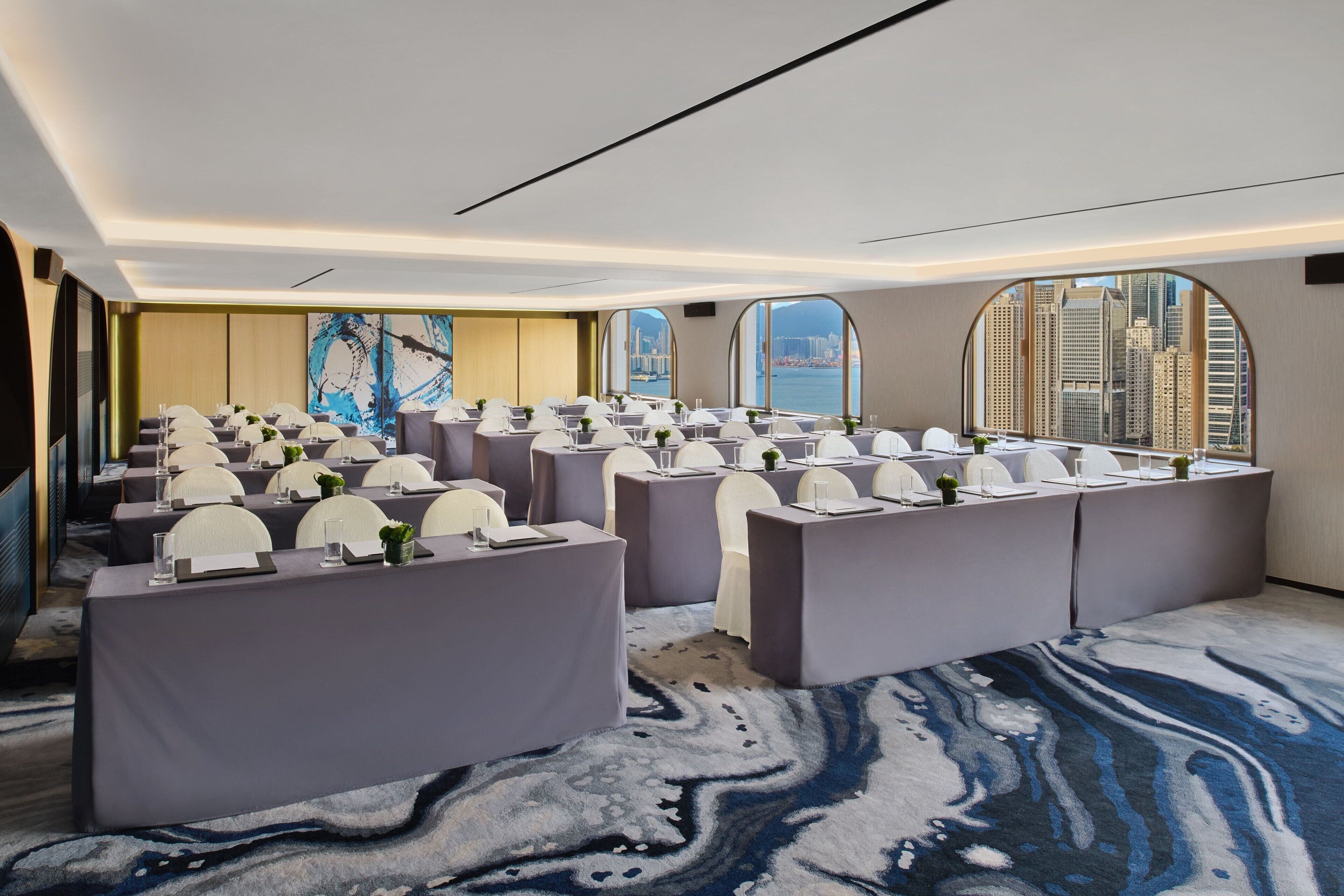 A conference room with tables and chairs, large windows with a city view, and a patterned carpet.
