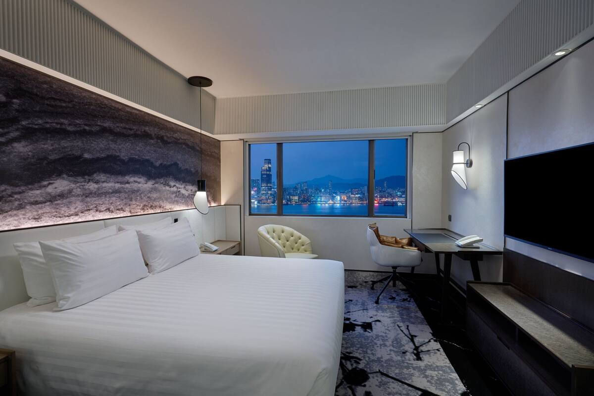 A modern hotel room with a large bed, a desk, a chair, and a TV.