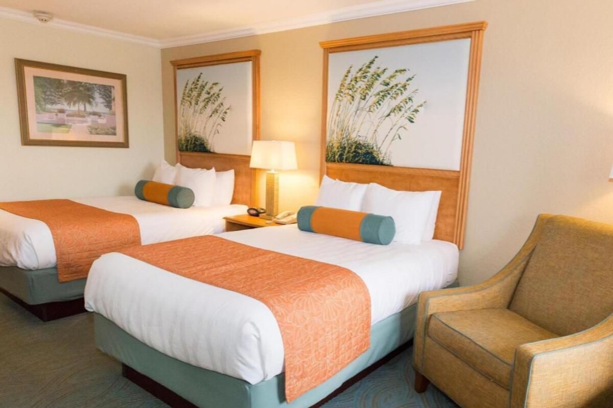 A hotel room with two beds, a chair, and artwork on the walls.