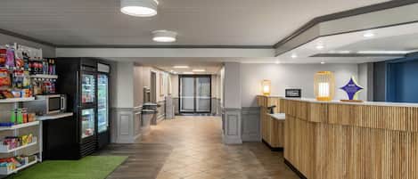 A hotel lobby with a reception desk, a refrigerator with beverages, and a microwave.