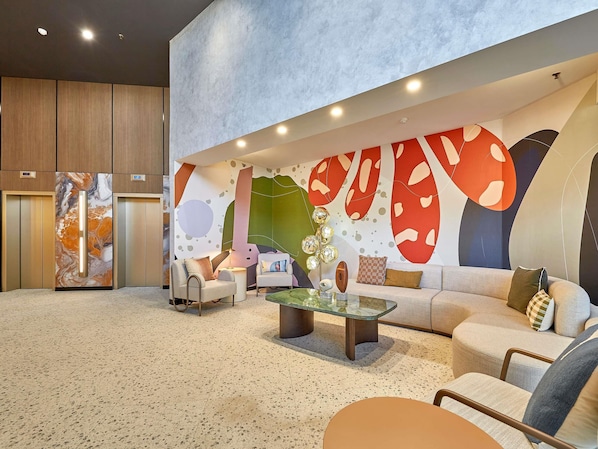 A modern living room with a large abstract mural, a sofa, two armchairs, a coffee table, and a glass-top table.