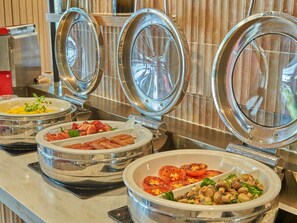 A buffet with various dishes including eggs, bacon, tomatoes, and mushrooms.