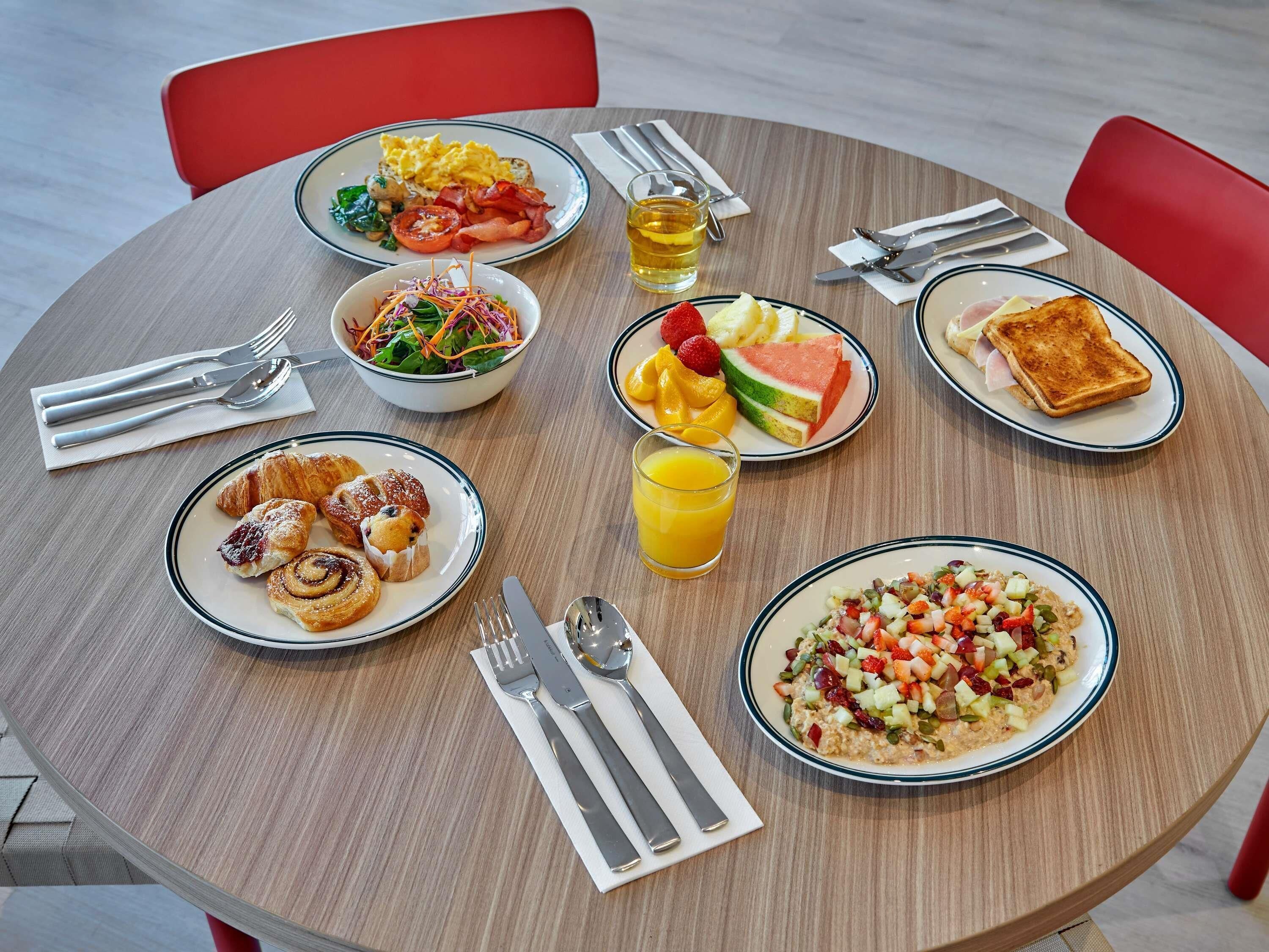 Una mesa redonda con diferentes alimentos para el desayuno, como huevos, tostadas, fruta y una ensalada.