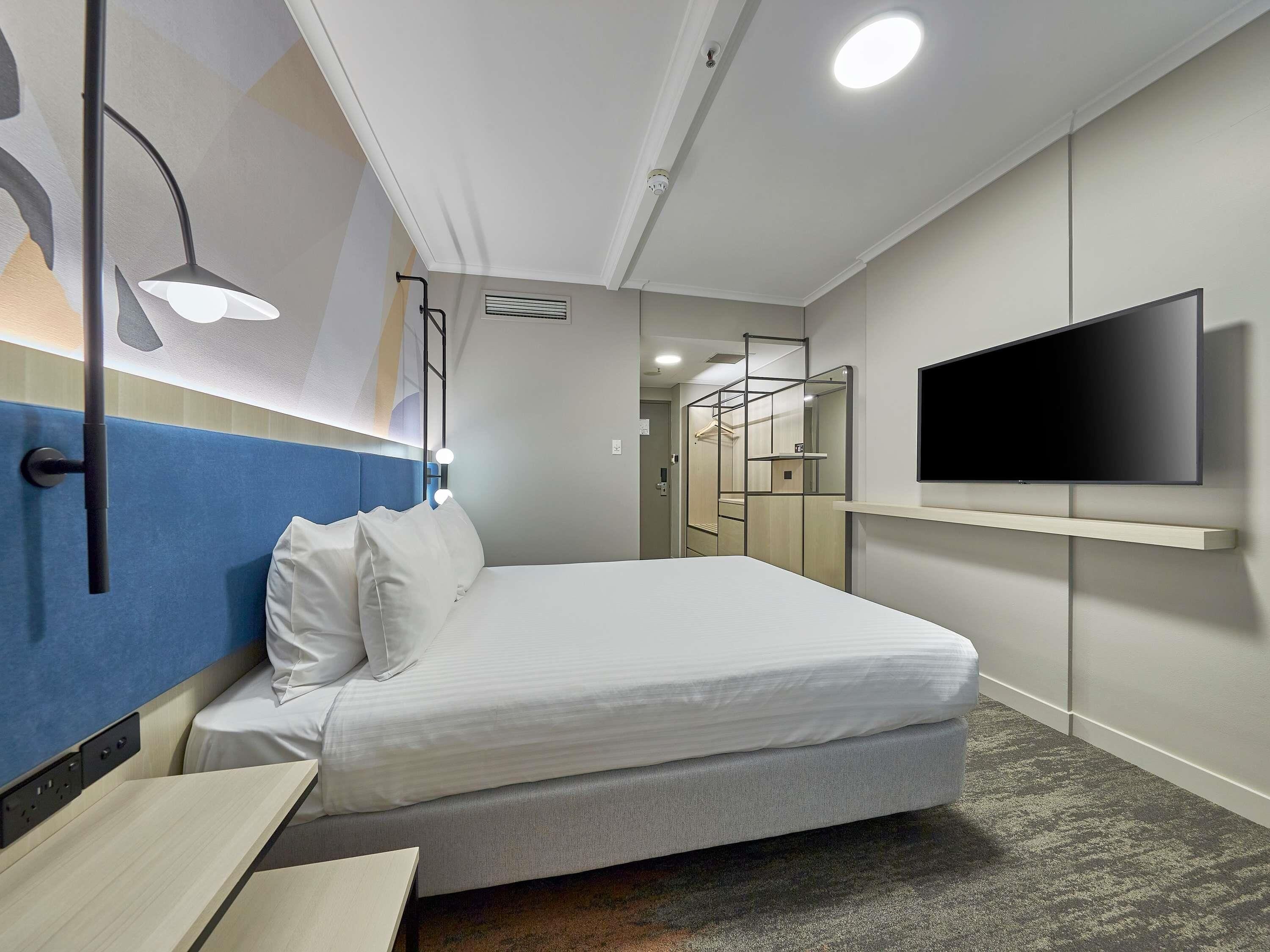 Een moderne hotelkamer met een bed, een bureau, een aan de muur bevestigde televisie en een spiegel.