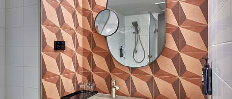 A bathroom with a geometric patterned wall, a round mirror, a shower, and a sink.