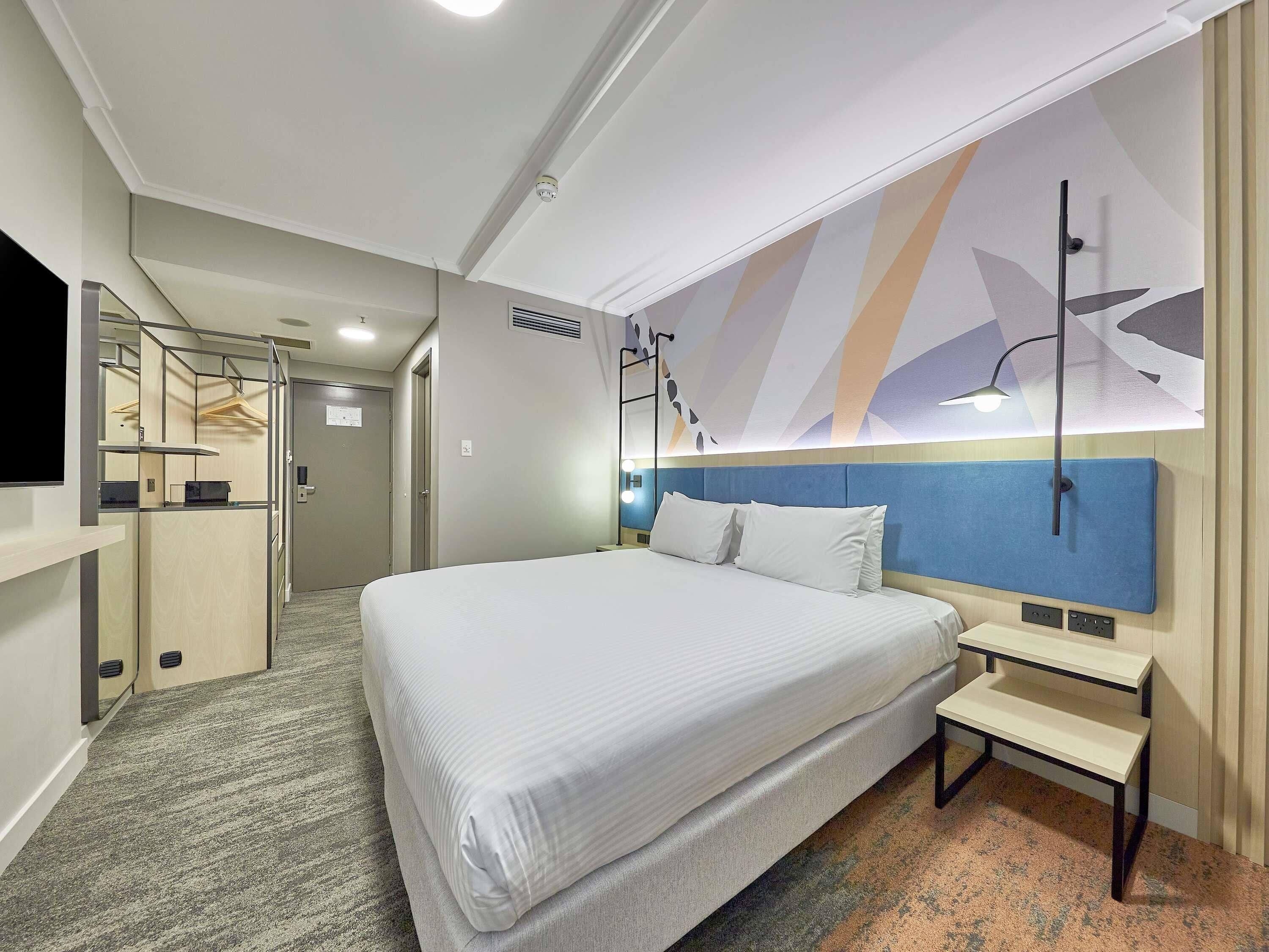 A hotel room with a large bed, a bedside table, a wall-mounted TV, and a ceiling light.