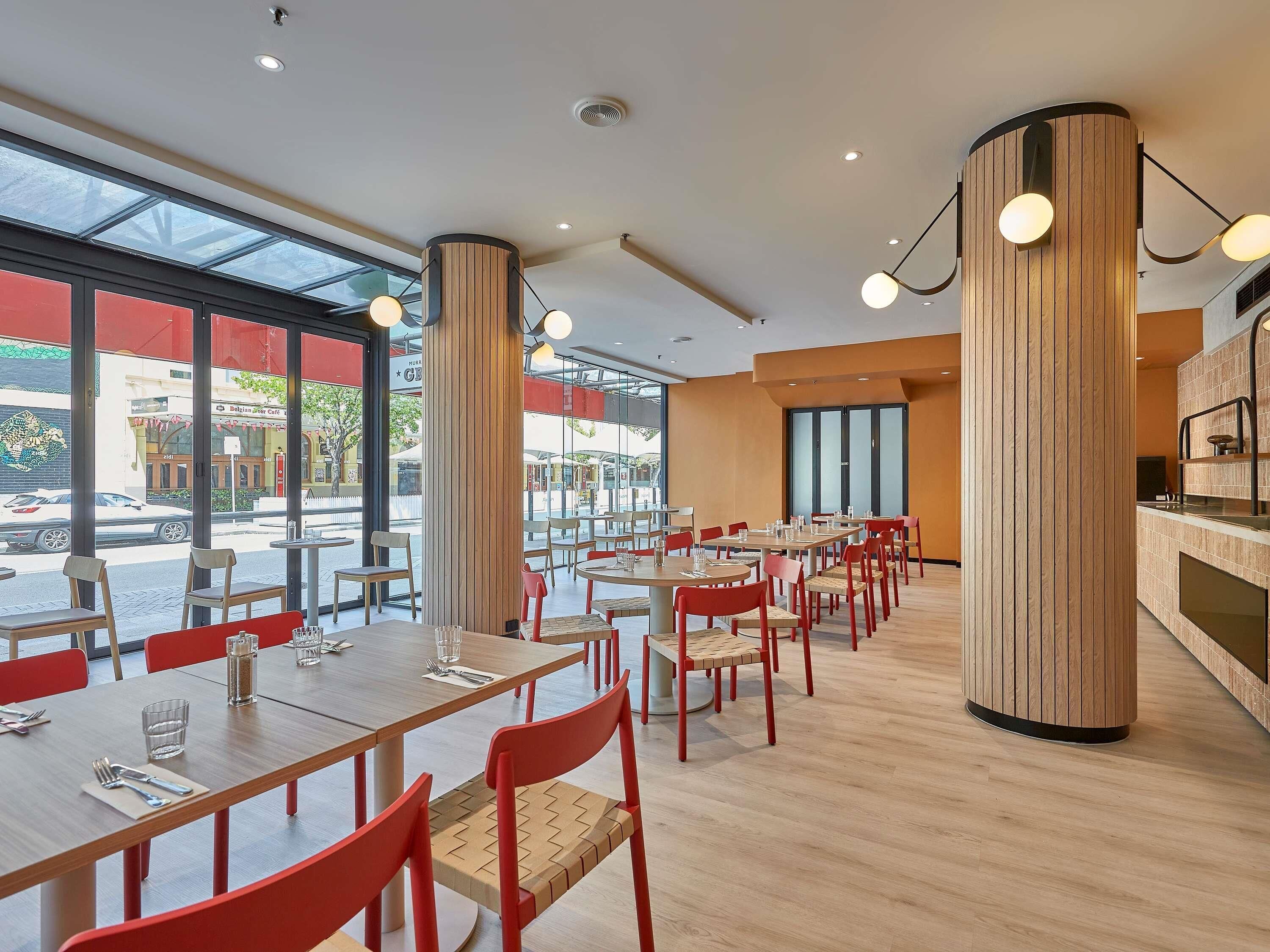 Un restaurante moderno con suelos de madera, sillas rojas y grandes ventanales con vistas a la calle.