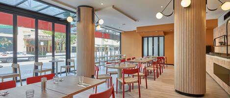 Un restaurante moderno con suelos de madera, sillas rojas y grandes ventanales con vistas a la calle.