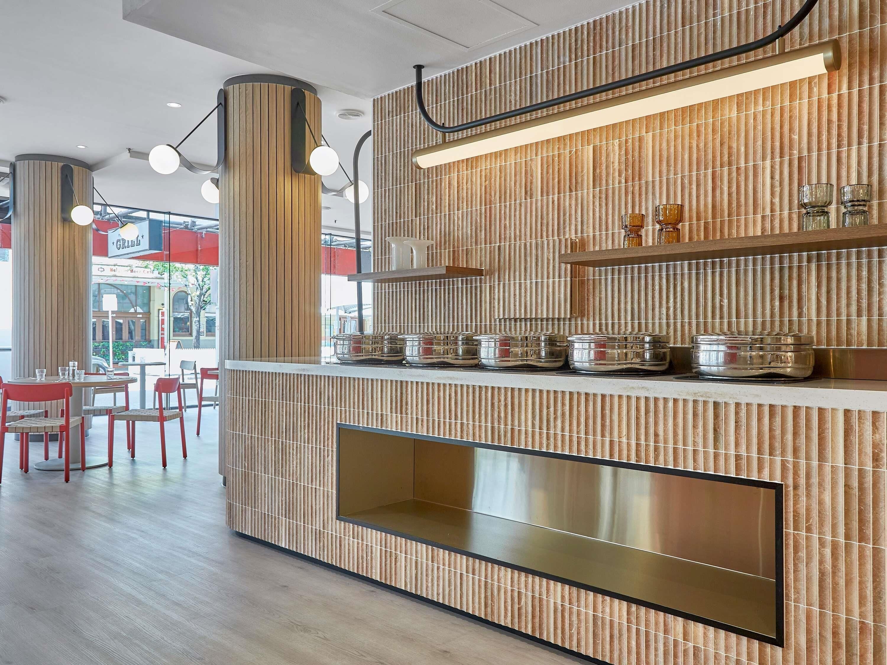 Ein modernes Restaurantambiente mit Holzvertäfelung, einer Theke mit Gläsern und roten Stühlen.