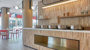 A modern restaurant interior with wooden paneling, a counter with jars, and red chairs.