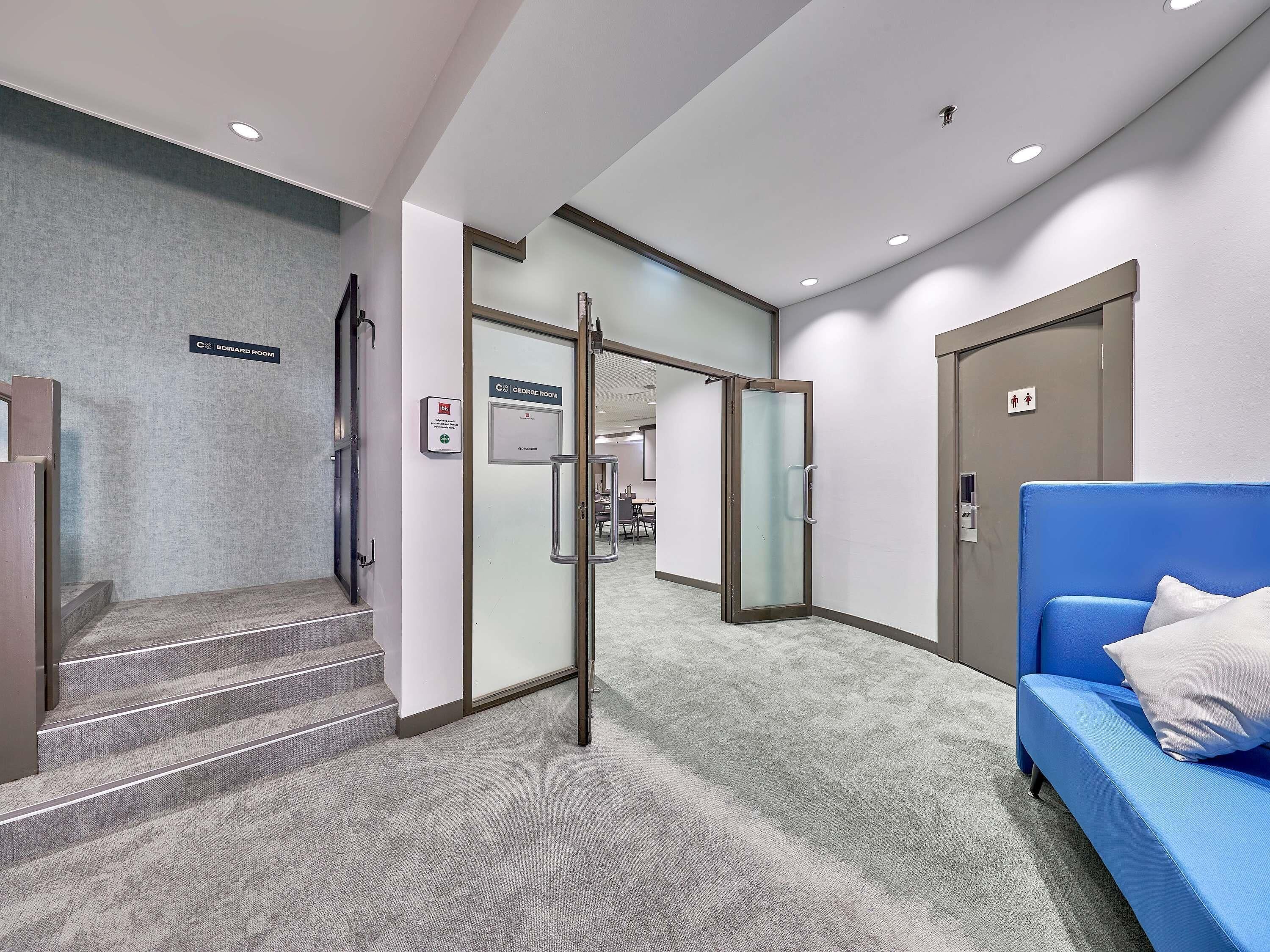 A hotel lobby with a blue sofa, a staircase, and a sign indicating the Edward Room.
