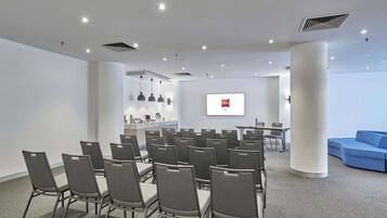 Ein Konferenzraum mit grauen Stühlen, einem weißen Tisch, einem Bildschirm mit dem ibis-Logo und einem blauen Sofa.