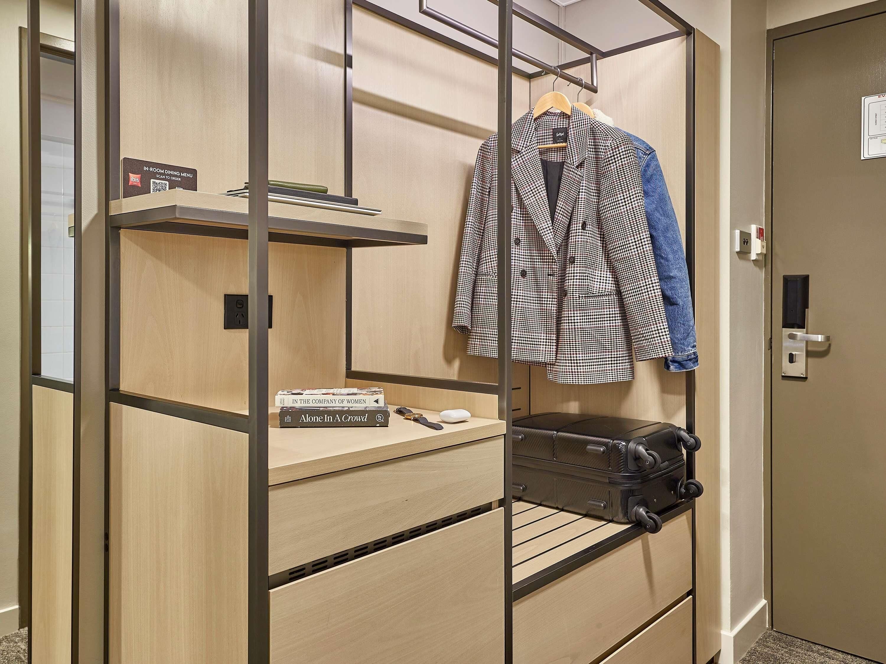 A hotel room with a wooden wardrobe, a hanging coat rack, and a suitcase on the floor.